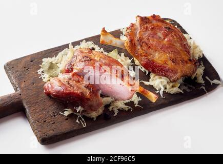 Geröstete deutsche Eisbein oder Schweinerücken auf einem Bett Sauerkraut serviert auf einem rustikalen Schneidebrett auf Weiß Stockfoto