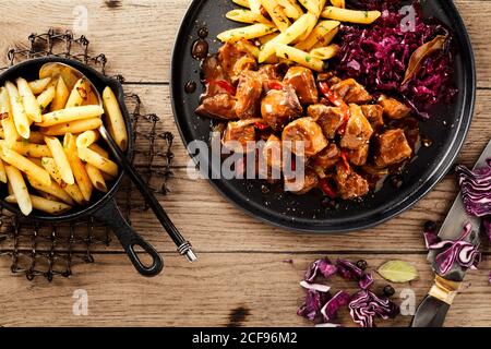 Servieren von scharfem Chilischef oder Wildgulasch mit Rot Kohl oder Sauerkraut und Seiten der Kartoffel Pommes in einem Overhead-Wohnung lag Blick auf ein rustikales Holz Stockfoto