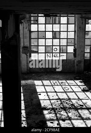 Schwarz-weiß leerer Raum des alten verlassenen Steingebäudes Mit schäbigen Wänden und Gitterfenstern mit Graffiti im Sonnenlicht Mit Schatten auf dem Boden Stockfoto