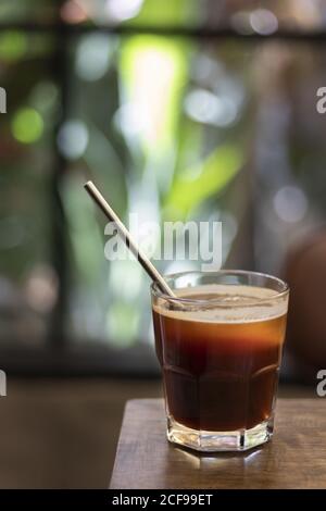 Vertikale selektive Fokusaufnahme eines Glases Eistschwarz Kaffee mit Metallstroh auf einem Kaffeetisch Stockfoto