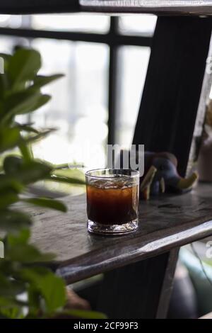 Vertikale selektive Fokusaufnahme eines Glases Eistschwarz Kaffee auf einem Kaffeetisch Stockfoto