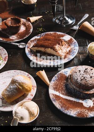 Hoher Winkel von Tiramisu garniert mit Kakaopulver platziert auf Tisch mit Muffin und Schokoladenkuchen bestreut mit Puderzucker Stockfoto