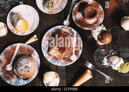 Hoher Winkel von Tiramisu garniert mit Kakaopulver platziert auf Tisch mit Muffin und Schokoladenkuchen bestreut mit Puderzucker Stockfoto