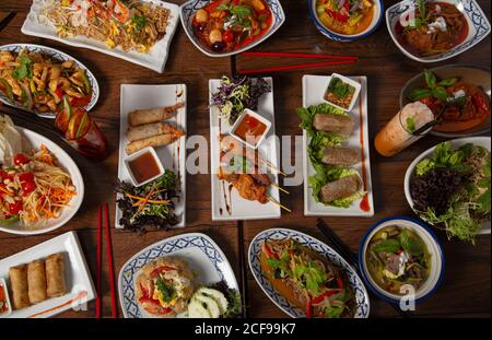 Von oben für verschiedene bunte würzige Thai-Essen serviert Familienessen auf Holztisch mit Essstäbchen Stockfoto