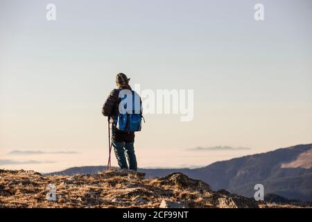 Rückansicht der anonymen Person mit Rucksack und Stöcken unterwegs Im trockenen Bergtal unter blauem Himmel bei strahlendem Sonnenschein Stockfoto