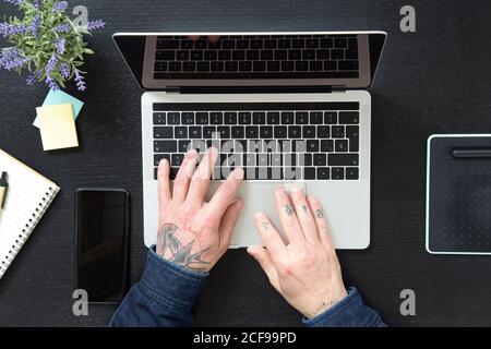 Von oben anonymen männlichen Eingabe auf Laptop-Tastatur während des Sitzens Am Tisch und arbeiten an Projekt in zu Hause während Quarantäne Stockfoto