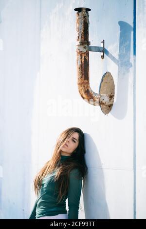 Volle Länge Seitenansicht der jungen barfuß weibliche Modell suchen Bei der Kamera posiert auf der Treppe in der Nähe der blauen Wand mit rostig Metallrohr Stockfoto