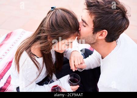 Oben fröhlich junges Paar in der lässigen Kleidung toasten mit Gläser Rotwein, während Sie gemeinsam glückliche Momente genießen Stockfoto