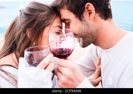 Oben fröhlich junges Paar in der lässigen Kleidung toasten mit Gläser Rotwein, während Sie gemeinsam glückliche Momente genießen Stockfoto