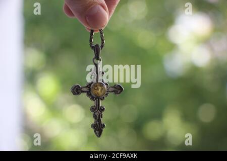 Frau Hand hält kleine silberne Kreuz mit verschwommener grüner Natur Hintergrund Stockfoto