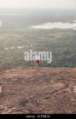 Von oben auf der Reise weiblich in legerer Kleidung bergauf laufen Auf dem Hintergrund des Tales mit Wald und See im Sommer Urlaub in Sigiriya Stockfoto