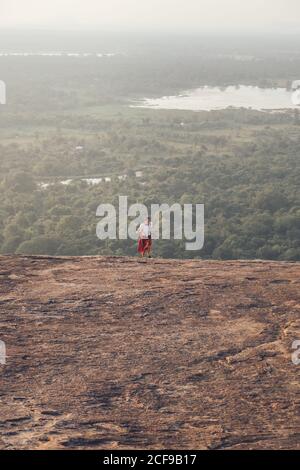 Von oben auf der Reise weiblich in legerer Kleidung bergauf laufen Auf dem Hintergrund des Tales mit Wald und See im Sommer Urlaub in Sigiriya Stockfoto