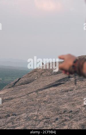 Unkenntlich Ernte männlichen Reisenden mit Armbändern auf der Hand Zeigefinger In der Ferne Bergadler auf Klippe während Sonnenuntergang Zeit stehen Am Sommerabend in Sri Lanka Stockfoto