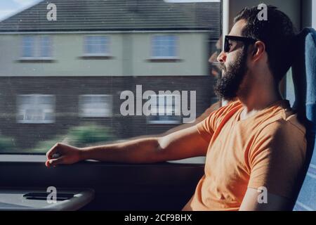 Nachdenklicher junger bärtiger Mann, der durch das Fenster schaute, während er vorbei reiste Trainieren Stockfoto