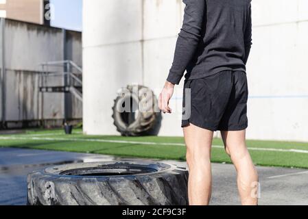Rückansicht der Ernte unkenntlich junge sportliche männliche Heben schwer Reifen auf Sportplatz Stockfoto