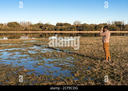 Seitenansicht eines nicht erkennbaren Mannes, der durch ein altes Fernglas schaute Die Fauna einer Lagune in Spanien Stockfoto