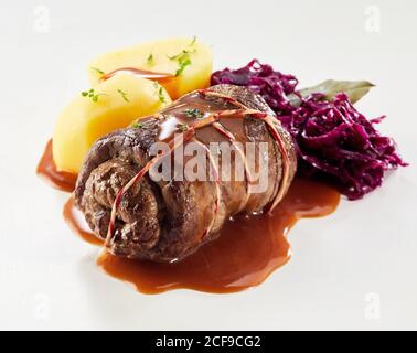 Einzelne Rinderroulade mit Rotkohl und Kartoffel garniert Kräuter und Soße isoliert auf Weiß für ein Menü Stockfoto