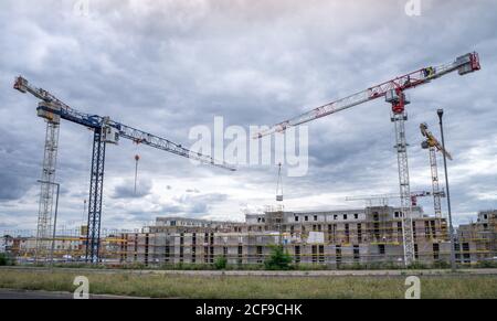 BERLIN, DEUTSCHLAND - 14. Mai 2020: BERLIN, DEUTSCHLAND 14. Mai 2020. Zwei Baukräne überqueren hinter einem Gebäude und dramatische Wolken im Hintergrund Stockfoto