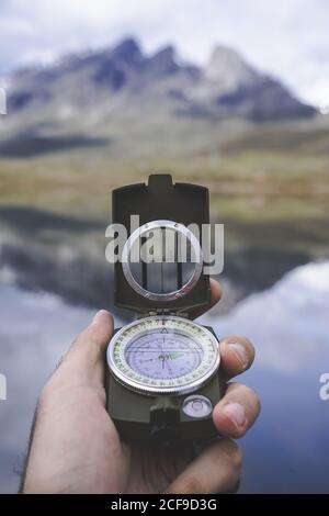 Hand des anonymen Reisenden mit Kompass gegen ruhigen Bergsee An bewölktem Tag in spanischer Landschaft Stockfoto