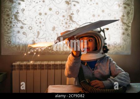 Fantasizing Junge in Astronaut Helm spielen mit Papier Flugzeug an Zu Hause Stockfoto