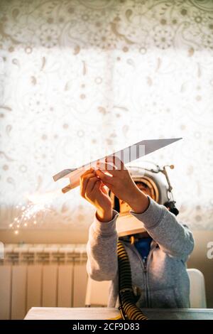 Fantasizing Junge in Astronaut Helm spielen mit Papier Flugzeug an Zu Hause Stockfoto