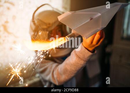 Fantasizing Junge in Astronaut Helm spielen mit Papier Flugzeug an Zu Hause Stockfoto