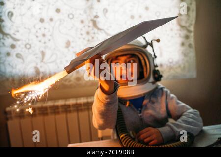 Fantasizing Junge in Astronaut Helm spielen mit Papier Flugzeug an Zu Hause Stockfoto