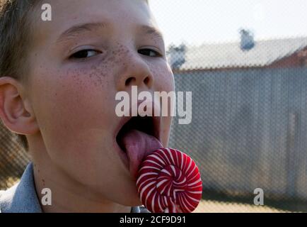 Der Junge isst einen leckeren Lollipop. Der Junge isst einen leckeren Lollipop. Der Junge leckt den Lutscher. Lollipop. Stockfoto