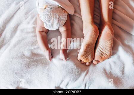 Draufsicht auf Ernte neugeborenes Baby in Windel liegend auf Bett mit Mutter im Haus Stockfoto