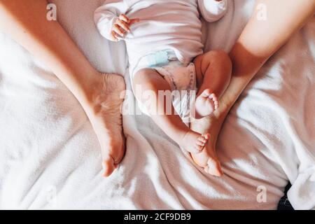 Draufsicht auf Ernte neugeborenes Baby in Windel liegend auf Bett mit Mutter im Haus Stockfoto