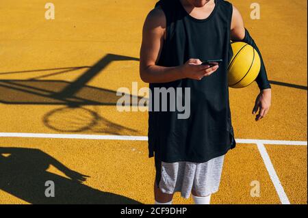 Männlicher Basketballspieler mit seinem Smartphone Ruhe nach dem Training Sitzung. Stockfoto