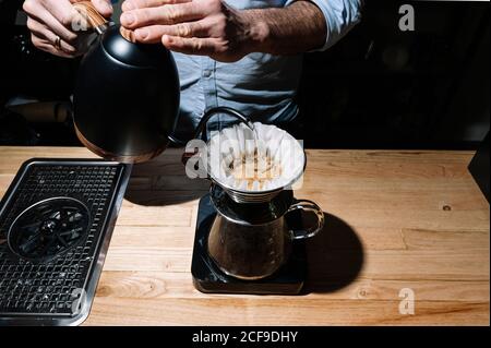 Von oben von anonymen männlichen Barista, der in der Nähe des Tisches stand Kaffee und Zubereitung von aromatischem Kaffee in der chemex-Kaffeemaschine Stockfoto