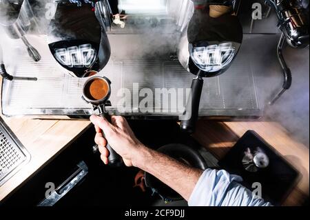 Von oben anonymer Barista, der im Stehen aromatischen Kaffee zubereitet In der Nähe professionelle Kaffeemaschine mit Portafilter im Café Stockfoto