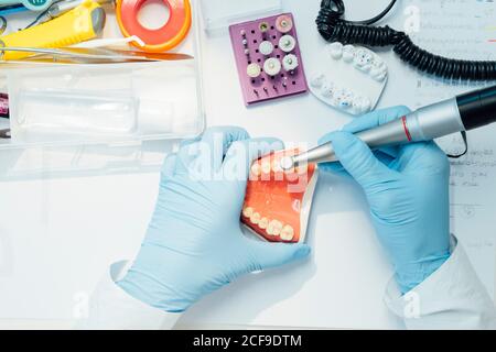 Von oben beschnitten anonymen Zahnarzt Trainee in blauen Handschuhen durchführen Zahnärztliche Operation mit Bohrer Carving Dental Guss während der Arbeit in Labor Stockfoto