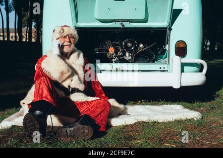 Älterer Mann im Kostüm des Weihnachtsmannes, der auf dem Handy spricht Telefon im Van mit offenem Motorraum Stockfoto