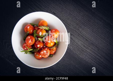 Von oben schmackhafte, appetitliche Kirschtomaten mit grünem Spargel sautiert Und Rosmarin in weißem Teller auf grauem Hintergrund Stockfoto