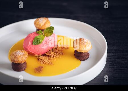 Von oben frisches kaltes Himbeer-Eis mit heilbaren Orangen Schokolade und Blätterteig in weißem Teller auf grauem Hintergrund Stockfoto