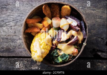 Draufsicht auf Bio-vegane Mahlzeit mit Mais, Tempeh-Protein und Gemüse in Kokos-buddha-Schüssel serviert. Stockfoto