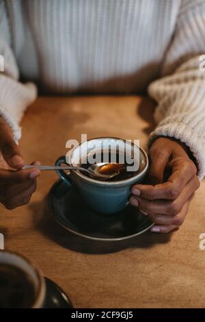 Oben die Hände der nicht erkennbaren Frau, die bei hölzern sitzt Tisch mit heißem Kaffee in einem rustikalen Becher Stockfoto