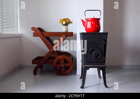 Landhaus-Design und Interieur mit Ofen. Roter Wasserkocher kocht auf einem Retro-Herd in der Küche. Konzentrieren Sie sich auf einen Ausguss Stockfoto