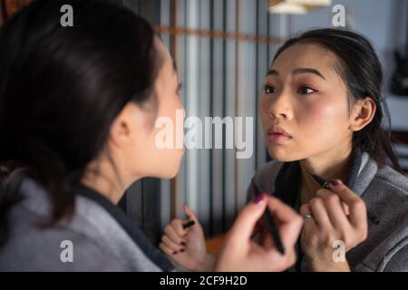 Asiatische Frau, die Eyeliner vor dem Spiegel anwendet Stockfoto