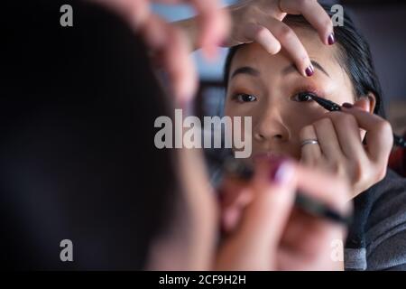 Asiatische Frau, die Eyeliner vor dem Spiegel anwendet Stockfoto