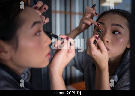 Asiatische Frau, die Eyeliner vor dem Spiegel anwendet Stockfoto