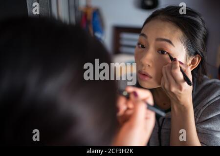 Asiatische Frau, die Eyeliner vor dem Spiegel anwendet Stockfoto