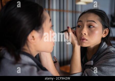 Asiatische Frau, die Eyeliner vor dem Spiegel anwendet Stockfoto