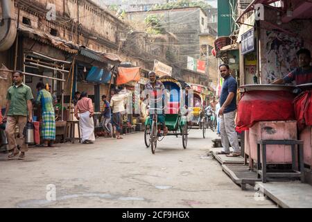 Bangladesch - Januar 20 2019: Traditionelle Rikschas mit ethnischen Männern und vollen Säcken, die auf Asphaltstraße durch Marktstraße in der Stadt reiten Stockfoto