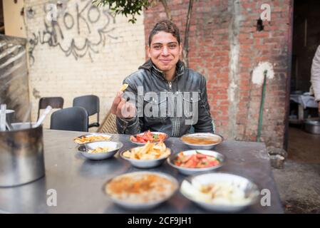 Kairo, Ägypten - 14. Dezember 2019: Ethnischer Mann mit Tragehege mit verschiedenen Gerichten serviert Kunden in Straßencafé Stockfoto