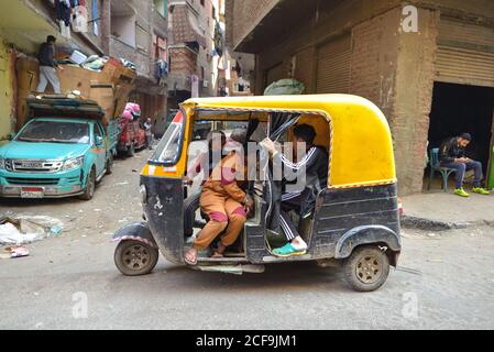 Kairo, Ägypten - 14. Dezember 2019: Seitenansicht von Einheimischen, die sich unterhalten, während sie Tuk Tuk Auto auf schmutziger Straße des armen Stadtteils fahren Stockfoto