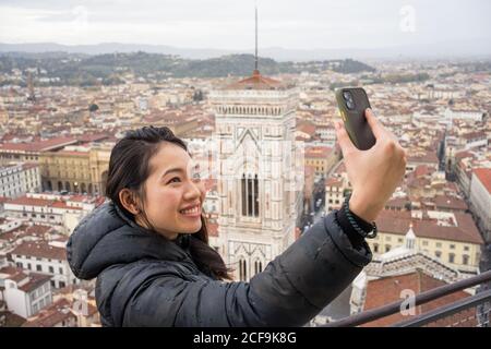 Glücklich asiatische Frau lächeln, die ein Selfie mit Handy Beim Stehen auf Brunelleschi Dome gegen alte Florenz Straßen während Urlaub in Italien Stockfoto