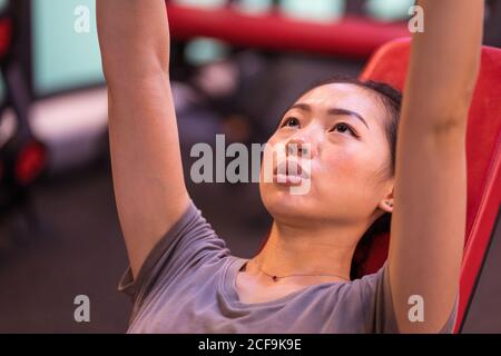 Leistungsstarke ethnische Athletin in Sportbekleidung tun Hanteln drücken auf Schrägbank mit Blick auf das moderne Fitnesscenter Stockfoto